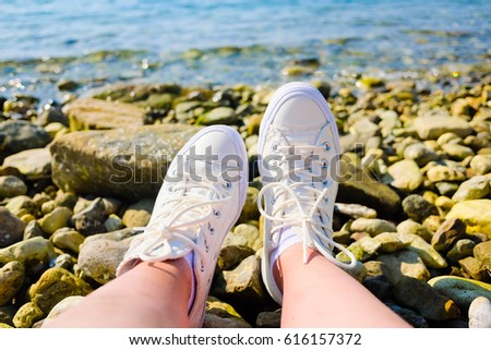 Feets in white sneakers over the sea