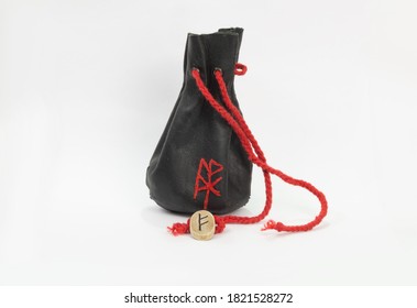 The Fehu rune is made of ash, an antique leather bag for Scandinavian runes on a white background.