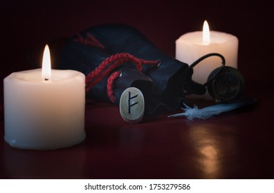 The Fehu rune is a symbol of wealth and pure well-being.
Fortune telling by candlelight: on the table is a bag with runes, a fallen rune and a feather on a background with bokeh.