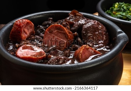 FEIJOADA served in a clay bowl on a rustic wooden table.