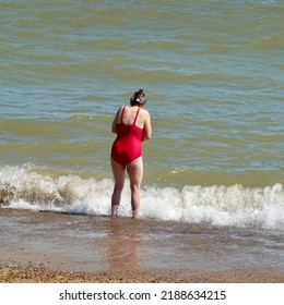 Felixstowe, Suffolk, UK - 10 August 2022 : Woman In A Red Swimsuit Paddling In The North Sea On A Hot Summer Day.