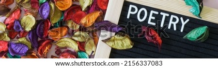 Felt board with the inscription poetry next to a lot of colorful dry leaves and petals. The concept of poetic creativity and diversity of genres. Autumn inspiration. Web banner. Close-up