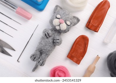 Felted cat, wool and different tools on white wooden table, flat lay