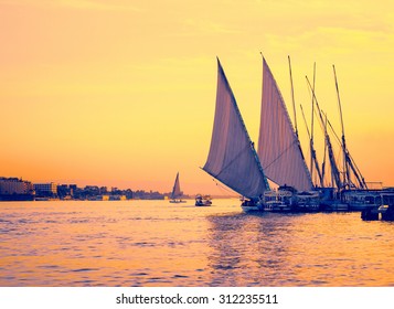 Feluccas At Sunset - Traditional Sail Vessel On Nile River In Egypt. Silhouettes Of Egyptian Sail Boats - Shoreline On The Nile In Evening.