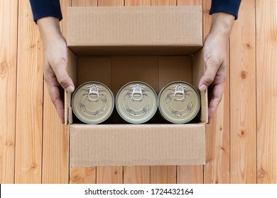 Femal Hands Holding A Cardboard Box Containing A Canned Food. Top View
