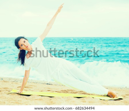 Female 20-30 years old is doing excercises on endurance on the beach near sea.