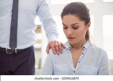 Female abuse. Nice cheerless unhappy woman sitting in the office and looking at the male hand while being sexually harassed