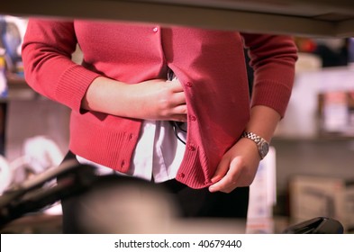 A Female In The Act Of Shoplifting Or Stealing Puts An Item Under Her Clothes