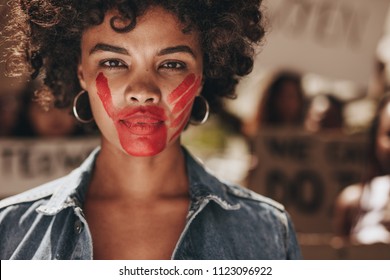 Female activist with a hand print on her mouth, demonstrating violence on women. Woman protesting against domestic violence and abuse with group in background.