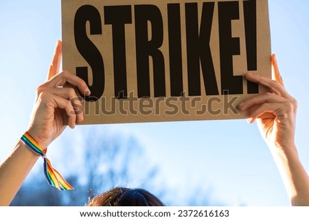 A female activist holding a sign with the slogan of the hollywood actors and writers strike with the blue sky in the background