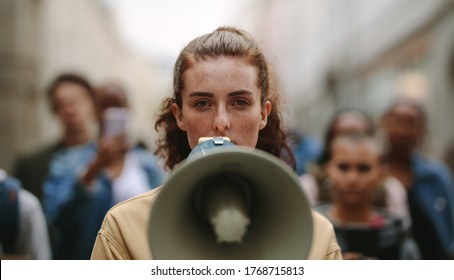Female activist protesting with megaphone during a strike with group of demonstrator in background. Woman protesting in the city. - Shutterstock ID 1768715813