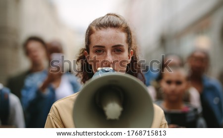 Female activist protesting with megaphone during a strike with group of demonstrator in background. Woman protesting in the city.