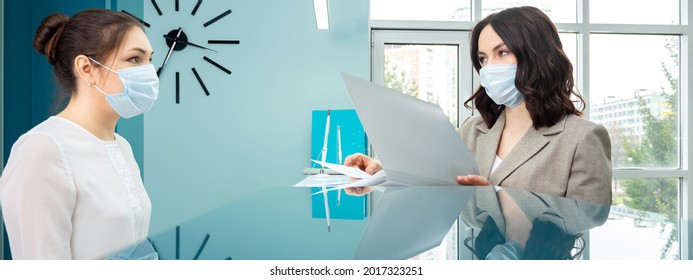 Female Administrator With Protective Mask In White Blouse Shows Registration Book To Woman Client Standing At Reception In Contemporary Hospital Close-up