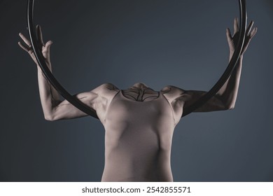 A female aerial hoop artist demonstrates poise and strength, gracefully balancing in the hoop. Her toned physique, tattoo, and expressive pose are highlighted against a dark studio backdrop - Powered by Shutterstock