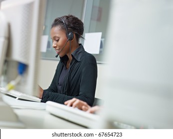 Female African American Customer Service Representative Talking On The Phone And Typing On Pc. Horizontal Shape, Side View, Copy Space