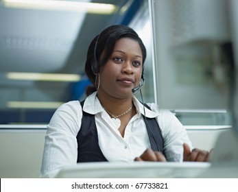 Female African American Customer Service Representative Talking On The Phone And Typing On Pc. Horizontal Shape, Front View