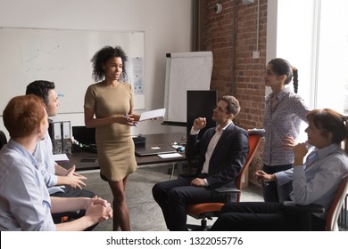 Female african american manager leader coach mentor speaking at diverse team stand up meeting, serious mixed race businesswoman speaker talking training teaching workers at group office workshop