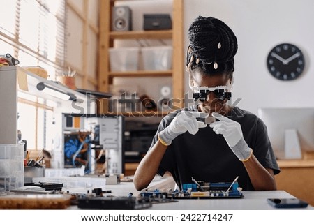 Female african american technician wearing glasses with binocular loupes attentively examining CPU