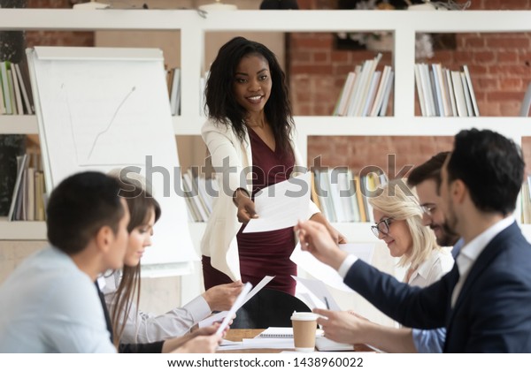 Female african coach manager give papers presenting\
document report business plan to team people at corporate meeting,\
diverse staff group and black boss do paperwork sit at office\
conference table