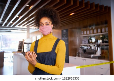 Female African Coffee Shop Owner Wearing Face Mask Standing In Front Of Counter With Digital Tablet.