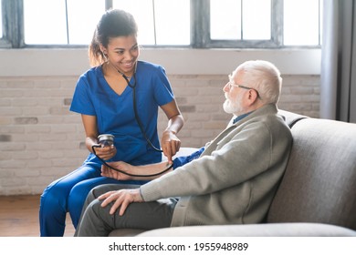 Female African Doctor Cardiologist Or Physician Checking High Blood Pressure Examining Old Male Patient Grandfather Using Tonometer During Home Medical Care Visit. Elderly Hypertension Cardiovascular.