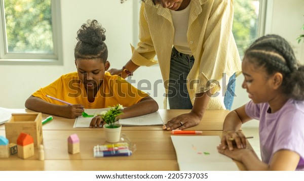A female African teacher is taking care of her\
young boy pupil in a class. A topknot kid gets close support from\
his teacher.