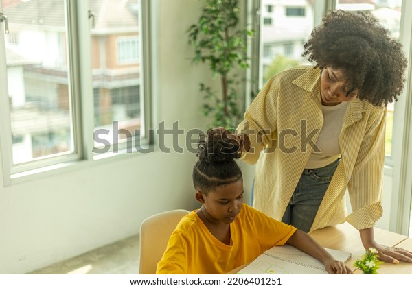 A female African teacher is taking care of her
young boy pupil in a class. A topknot kid gets close support from
his teacher.