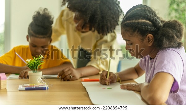 A female African teacher is taking care of her\
young boy pupil in a class. A topknot kid gets close support from\
his teacher.
