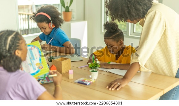 A\
female African teacher is taking care of her young kids in a class.\
A topknot kid gets close support from his\
teacher.