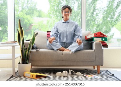 Female African-American graphic designer meditating on sofa in office - Powered by Shutterstock