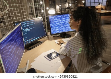 Female African-American programmer with computer monitors working in office at night, back view - Powered by Shutterstock