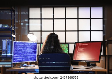 Female African-American programmer working with computer monitors in office at night, back view - Powered by Shutterstock