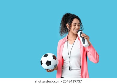 Female African-American soccer trainer with ball and water bottle on blue background - Powered by Shutterstock