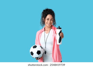 Female African-American soccer trainer with ball and water bottle on blue background - Powered by Shutterstock