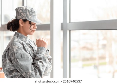 Female African-American soldier praying near window at headquarters - Powered by Shutterstock