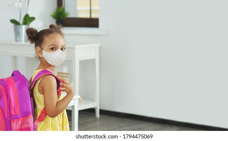 A Female African-American Student With A Medical Mask And School Backpack On Her Back, Came To Class For Lessons. Dark-skinned Girl Student In A Yellow Dress With A Respiratory Protection Mask