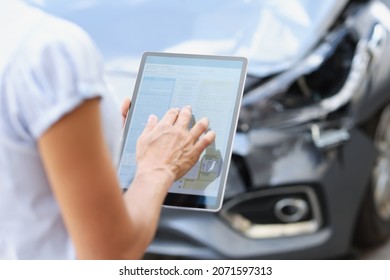 Female Agent Filling Out Insurance Claim On Digital Tablet Against Background Of Broken Car Closeup. Car Insurance Modern Technologies Concept