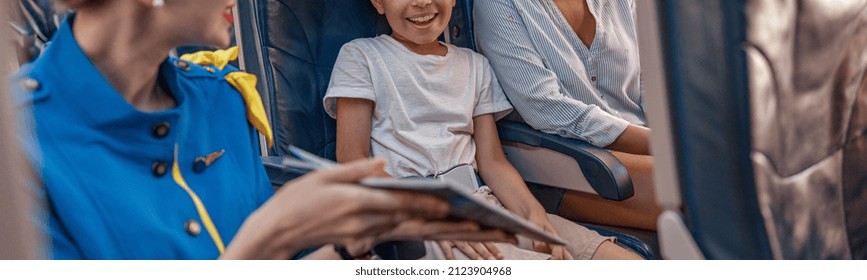 Female Air Hostess Trying To Entertain A Kid On The Plane By Offering A Book To Read. Cabin Crew Provide Service To Family In Airplane. Airline Transportation And Tourism Concept