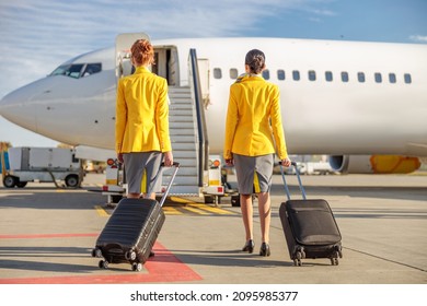 Female airline workers carrying travel bags at airport - Shutterstock ID 2095985377