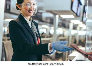 Female Airport Staff Wearing Face Shield Assisting Travelers. Woman Working At Airline Check-in Counter During Pandemic. 