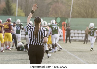 Female American Football Referee Giving Signals And Blurred Players In The Background