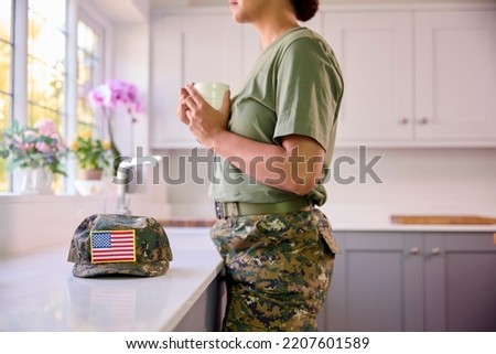Female American Soldier In Uniform In Kitchen On Home Leave Looking Out Of Window Drinking Coffee