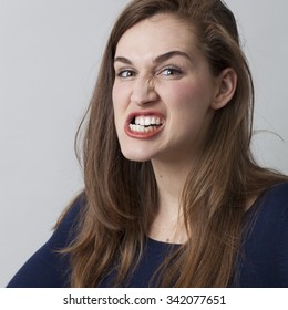 female anger concept - angry beautiful 20s girl grinding her teeth threatening someone,showing aggressiveness,closeup in studio