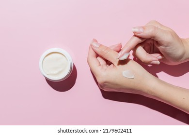 Female Applying A Collagen Firming Cream To A Hand. Open Cream Jar On Pink Background. Cosmetics Mockup. Trendy Colors And Shoot