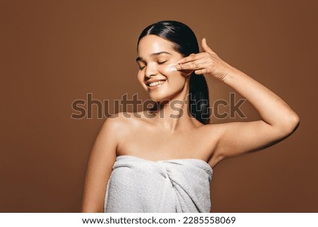 Female applying facial cream in a studio. Beautiful Hispanic woman pampering her skin using moisturizing lotion, enjoying practicing a healthy skincare routine for a radiant complexion.