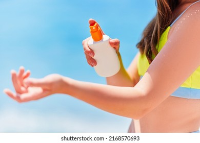 Female applying and holding white empty bottle blank of sunscreen spray cream while sunbathing on beach by the sea in sunny summer day. Sun protection