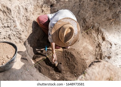 Female archaeologist digging up ancient pottery object at an archaeological site.