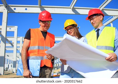 Female architect, construction engineer and manager talking about the project on construction site. Teamwork and people concept - group of builders and architect in hardhats, positive emotions