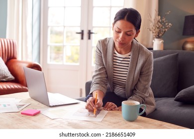 Female Architect Or Interior Designer Working From Home Looking At Designs On Laptop