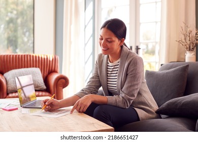 Female Architect Or Interior Designer Working From Home Looking At Designs On Laptop